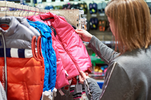 Buyer woman chooses kid jacket clothes in store