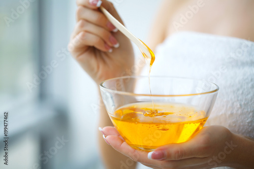 Women hold orange paraffin wax bowl. Woman in beauty salon