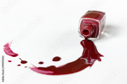Red nail polish is poured from the vial. White background. Creative art. Place for text