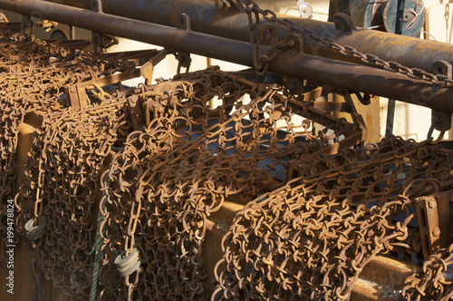 Rusty chains used for raking the sea-bed to disturb flatfish hanging over the edge of a fishing trawler boat. photo