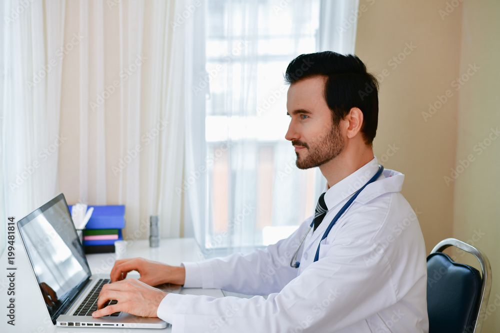Smiling doctor posing in the office, he is wearing a stethoscope, medical staff on the hospital background Smiling doctor posing in the office, he is wearing a stethoscope, medical staff on the hospital background