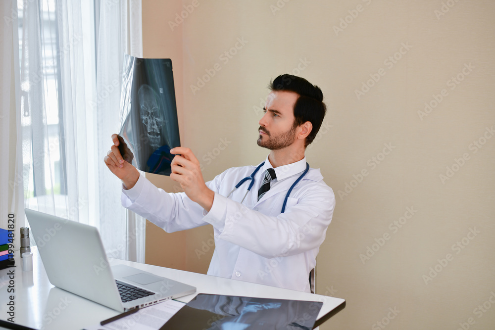 Smiling doctor posing in the office, he is wearing a stethoscope, medical staff on the hospital background Smiling doctor posing in the office, he is wearing a stethoscope, medical staff on the hospital background
