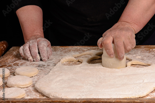 Granny squeezes a glass of a circle in a dough on the table photo