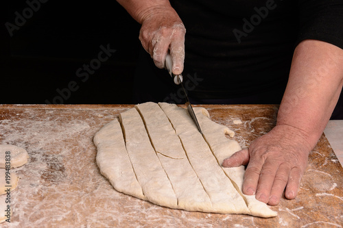 The cook slicers raw dough with a knife on a narrow line photo