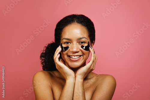 Young smiling woman applying face patch with hands, front view