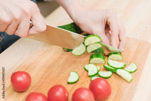 close-up of female hands cut into fresh cut cucumbers on a wooden cutting board next to pink tomatoes. The concept of homemade vegetarian cuisine and healthy eating and lifestyle
