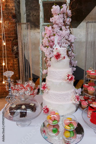White three-level wedding cake decorated with flowers and greens with deserts in the foreground. Wedding. Ceremony photo