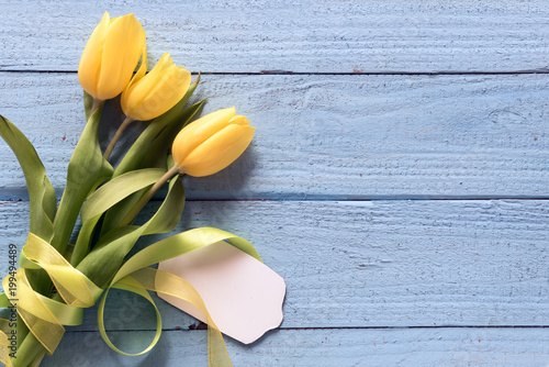 Fototapeta Naklejka Na Ścianę i Meble -  yellow tulip flowers and a blank card on a blue wooden background with copy space, top view from above