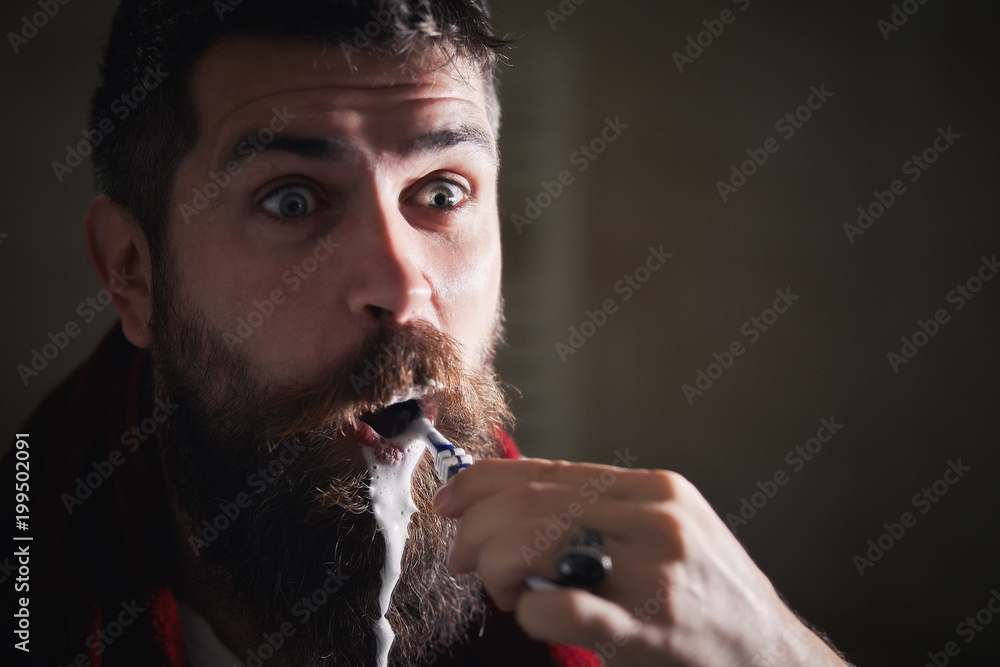 Silly bearded man brushing teeth in bathroom mirror. Young man at home ...