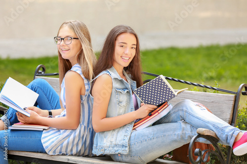 Two happy teen girls reading books on park bench, youth education and friendship, outdoor learning and student lifestyle