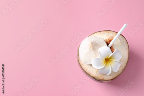 Fresh green coconut with drinking straw and flower on color background, top view