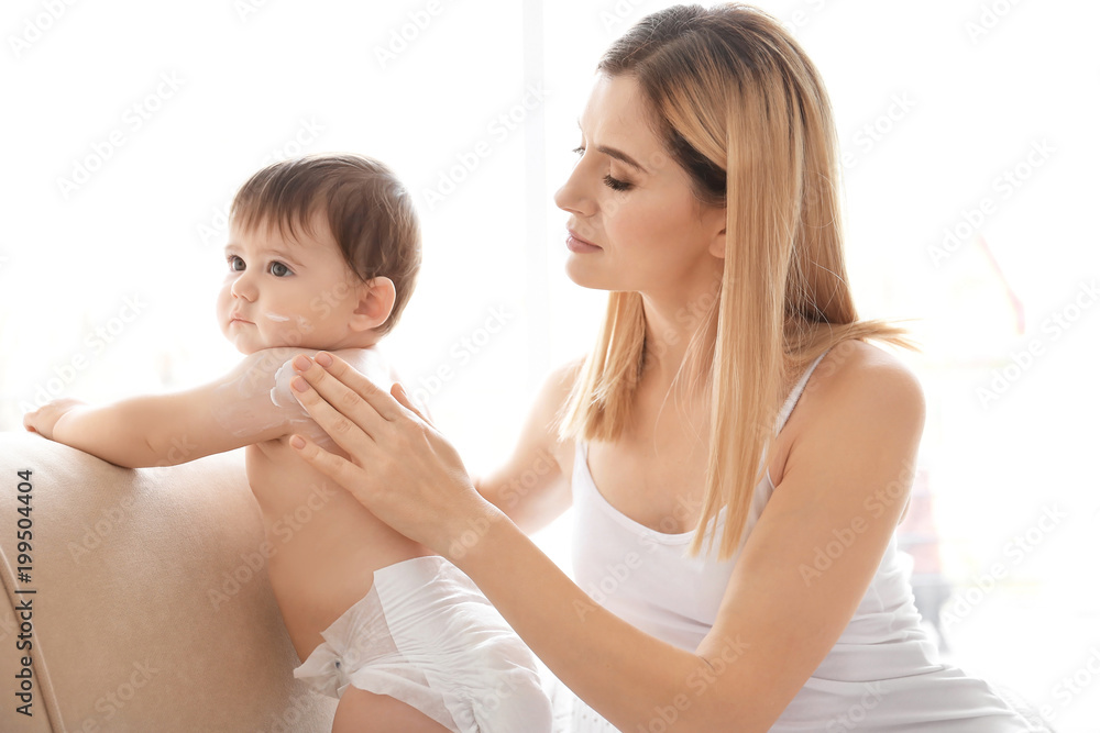 Woman applying body cream on her baby indoors Woman applying body cream on her baby indoors