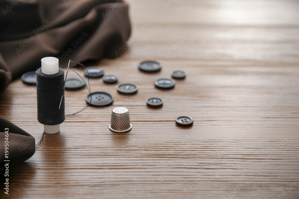 Thread, thimble and buttons for tailoring on wooden background Thread, thimble and buttons for tailoring on wooden background