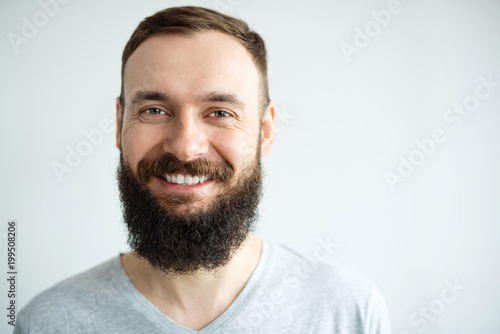 Portrait of a beautiful real hipster man teeth smile with a full face of a beard and mustache on a light background in a barber shop