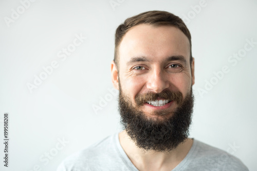 Portrait of a beautiful real hipster man teeth smile with a full face of a beard and mustache on a light background in a barber shop