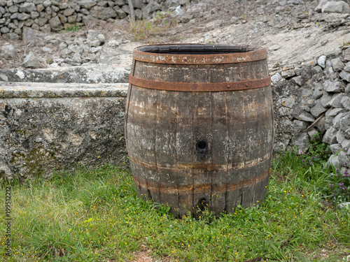 Old wine barrel standing on a meadow near a stone wall
