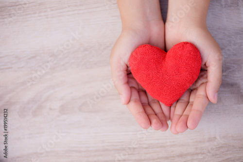 Health care  love  organ donation  family insurance and CSR concept. adult and child hands holding handmade red heart on wooden background.