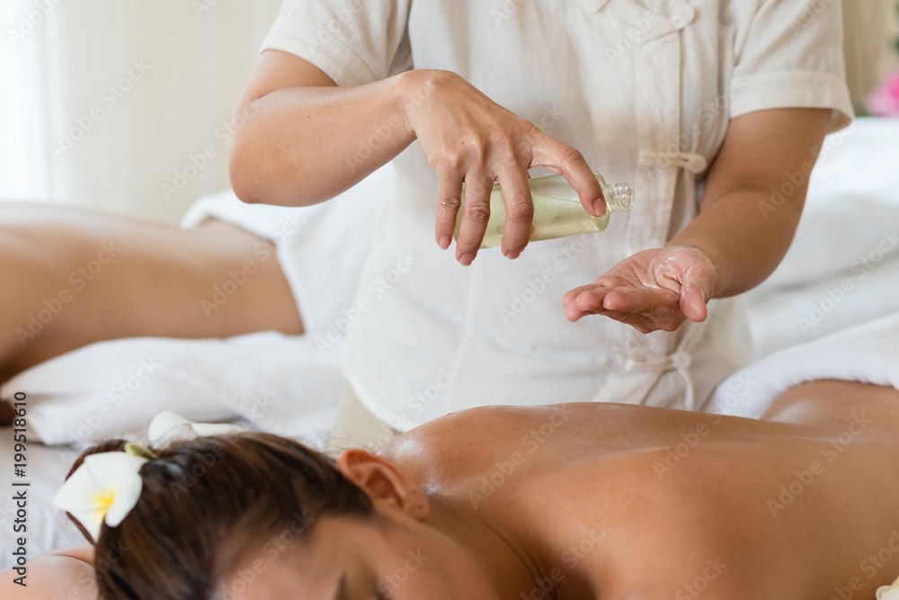 Masseuse pour oil on the hand and young asian woman relaxing receiving back massage at spa salon Masseuse pour oil on the hand and young asian woman relaxing receiving back massage at spa salon
