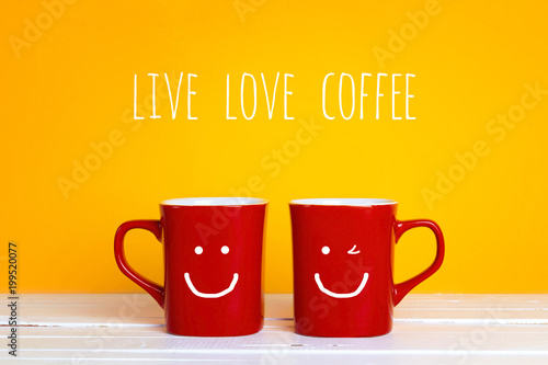 Two red coffee mugs with a smiling faces on a yellow background with the phrase Live Love Coffee.