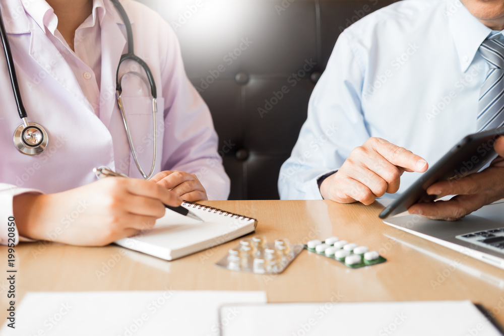 Two doctors discussing patient notes in an office pointing to a tablet as they make a diagnosis or decide on treatment Two doctors discussing patient notes in an office pointing to a tablet as they make a diagnosis or decide on treatment
