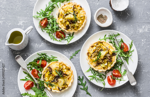 Vegetarian savory hands pie with porcini mushrooms, leeks, potatoes and arugula, tomatoes salad on grey background, top view. Mediterranean style lunch, snack, appetizer, breakfast
