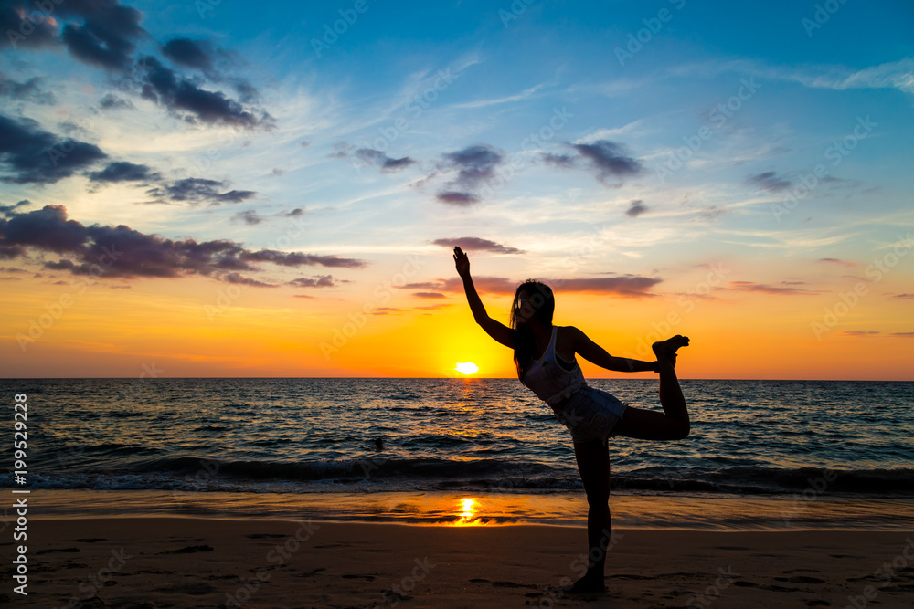 Young healthy women practicing yoga at sunset on beach