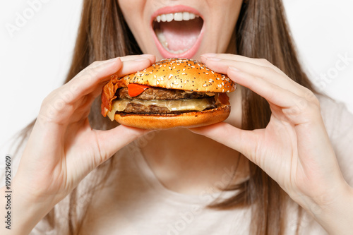 Close up cropped shot young woman holding in hands burger  trying to eat isolated on white background. Proper nutrition or American classic fast food. Copy space for advertisement. Advertising area.