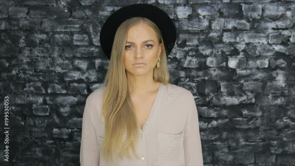 A girl in a black hat and a gray shirt posing against a brick wall background