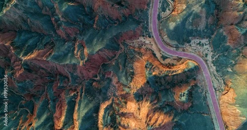 Aerial view on a curved, red road within orange sandstone hills covered with sparse vegetation. Unique, minimalistic landscape in Zhangye Danxia National Geopark, China.