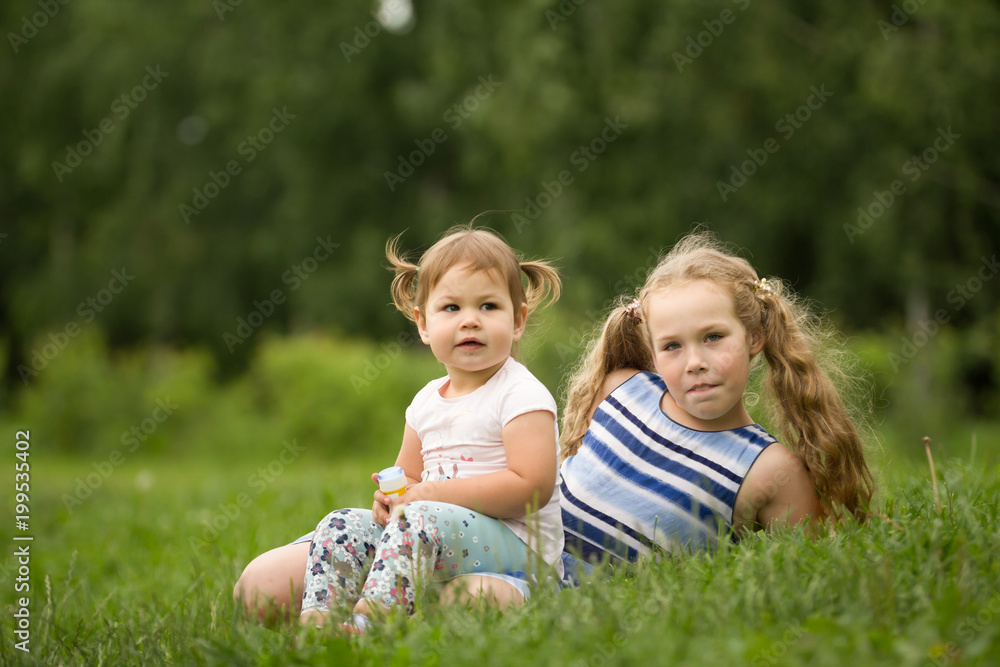 A portrait of two sisters on green grass, park outdoor A portrait of two sisters on green grass, park outdoor
