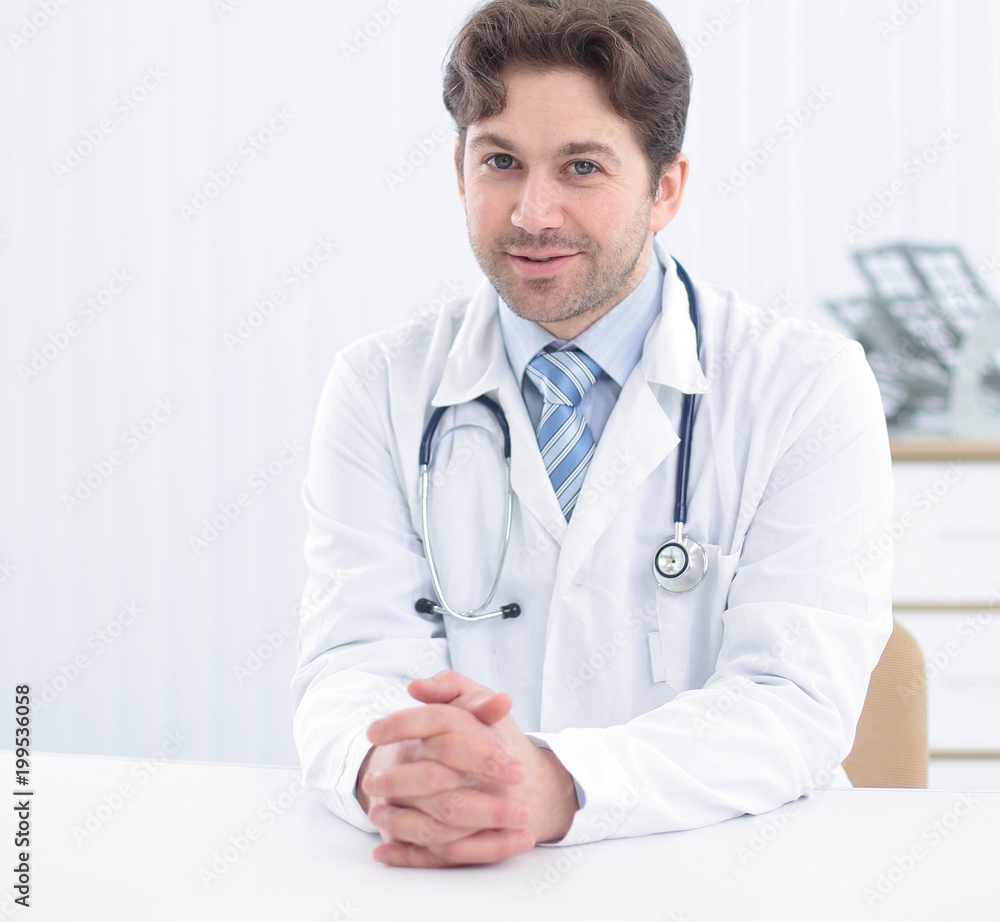 Handsome young doctor in white coat is looking at camera and smiling while standing in office Handsome young doctor in white coat is looking at camera and smiling while standing in office