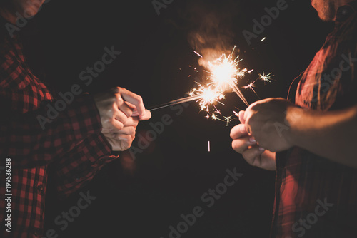 The happy couple hold a firework sticks. evening night time