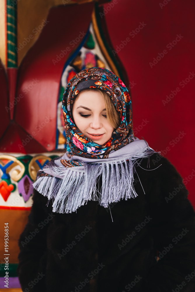 A young beautiful girl in a mink coat and a Russian folk scarf walks around the Izmailovo Kremlin. Moscow, Russia.