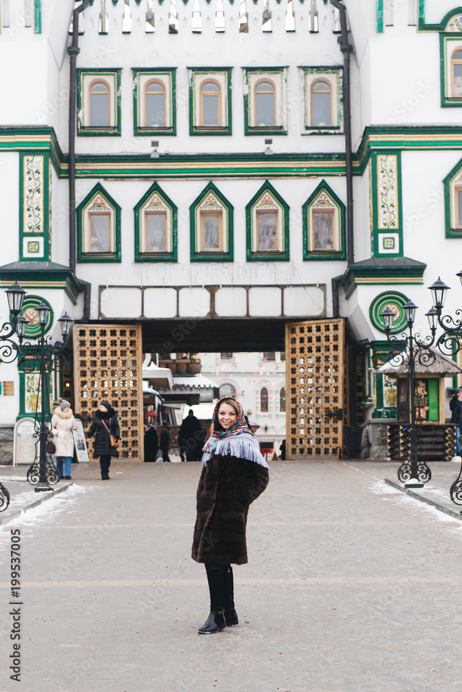 A young beautiful girl in a mink coat and a Russian folk scarf walks around the Izmailovo Kremlin. Moscow, Russia.