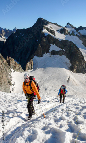 mountain guide and client heading up a glacier towards a high alpine summit on a beautiful summer morning