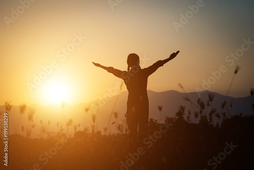 Silhouette of woman praying over beautiful sky background © Johnstocker