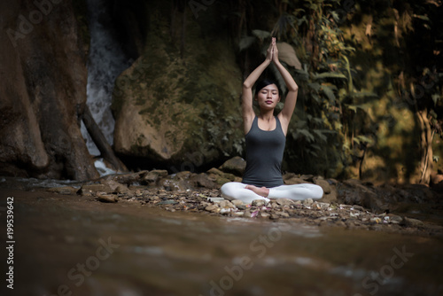 Young woman in yoga pose sitting near waterfall