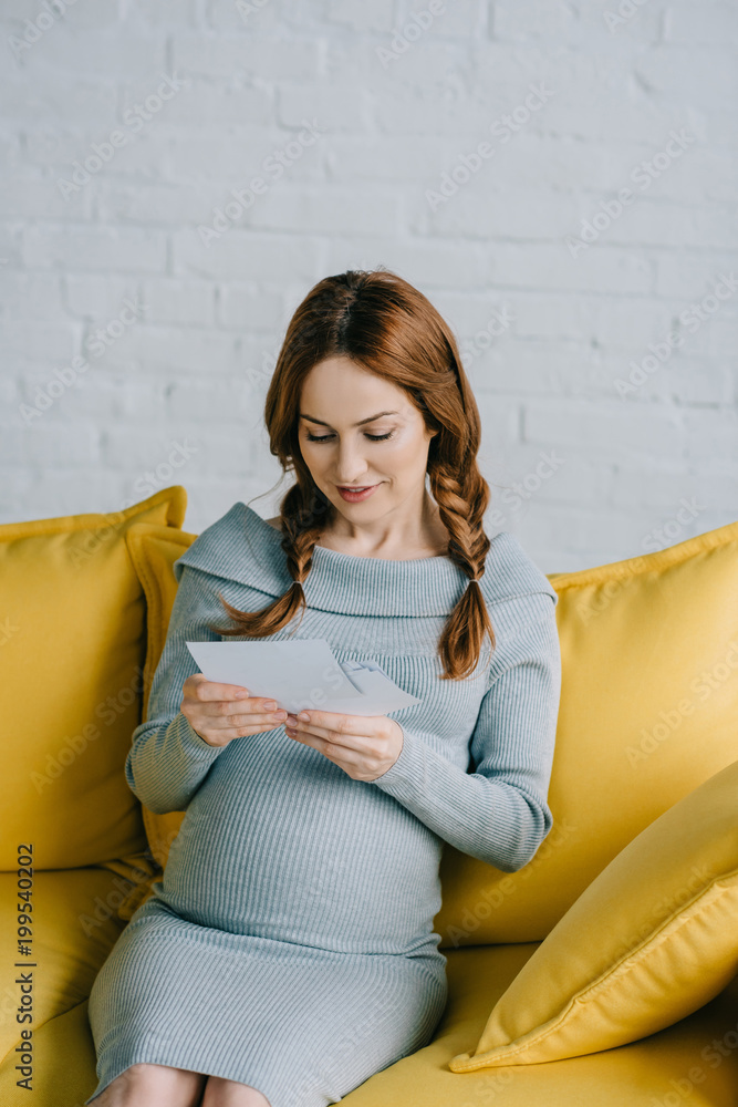 attractive pregnant woman sitting on sofa and looking at photos in living room attractive pregnant woman sitting on sofa and looking at photos in living room