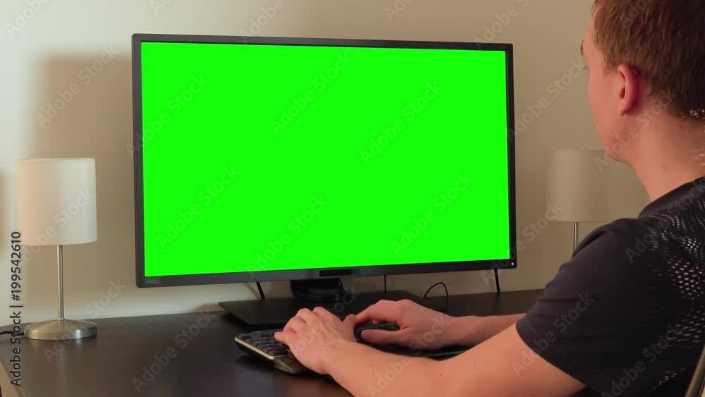 A man sits at a table and works on a computer with a green screen A man sits at a table and works on a computer with a green screen