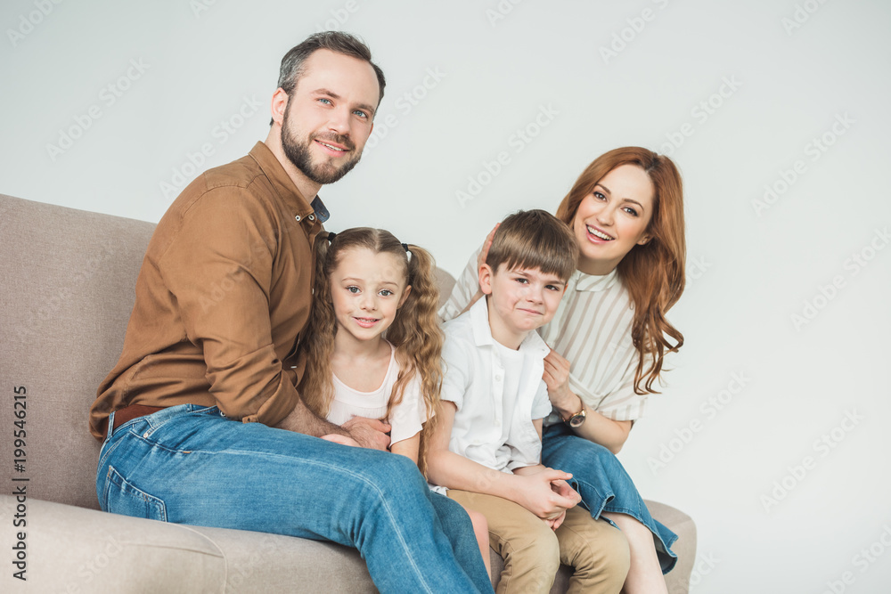 cheerful family with two children sitting on couch and smiling at camera on grey cheerful family with two children sitting on couch and smiling at camera on grey