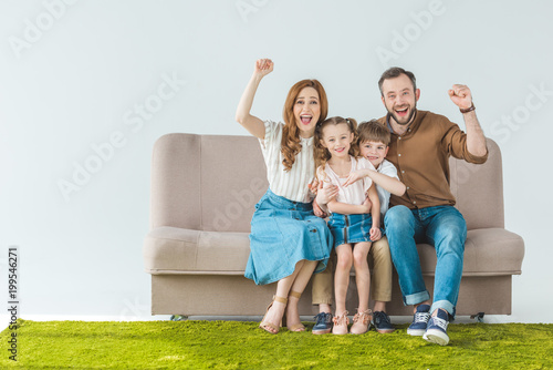 cheerful family wity two kids sitting on sofa and smiling at camera on grey photo