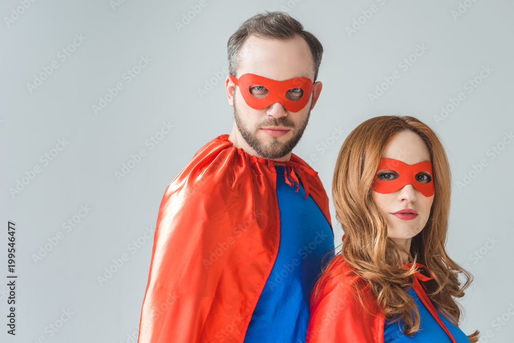 couple in superhero costumes standing together and looking at camera isolated on grey couple in superhero costumes standing together and looking at camera isolated on grey