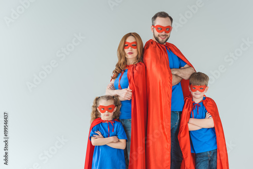 super family in masks and cloaks standing with crossed arms and looking at camera isolated on grey