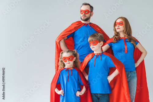 family of superheroes in costumes standing with hands on waist and looking away isolated on grey