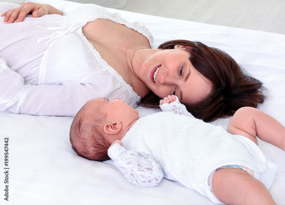 Mother and child lie together, look at each other with love. View from top above of affectionate mom and newborn. Young woman and her baby faces. Children and parents concept