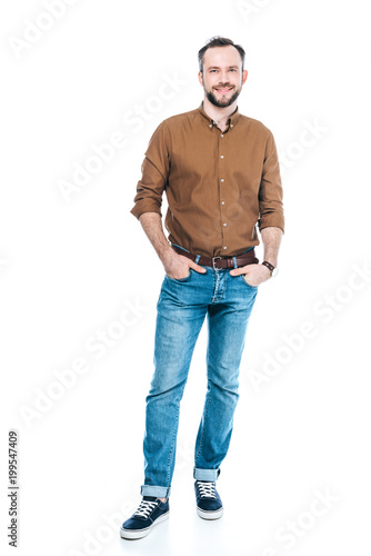 full length view of handsome bearded man standing with hands in pockets and smiling at camera isolated on white