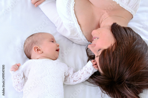 Mother and child lie together, look at each other with love. View from top above of affectionate mom and newborn. Young woman and her baby faces. Children and parents concept