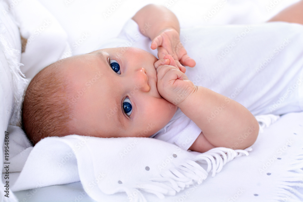 Newborn baby lying with open eyes in bed on white background