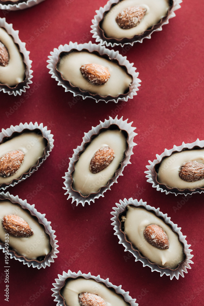 Flat lay of delicious praline sweets with almonds on red background