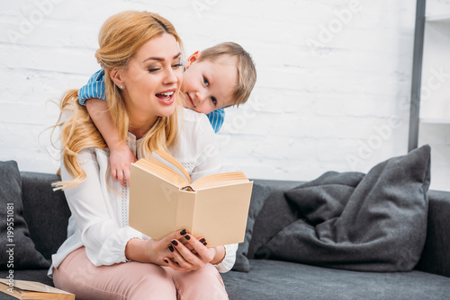 Little boy embracing mother while she reading book